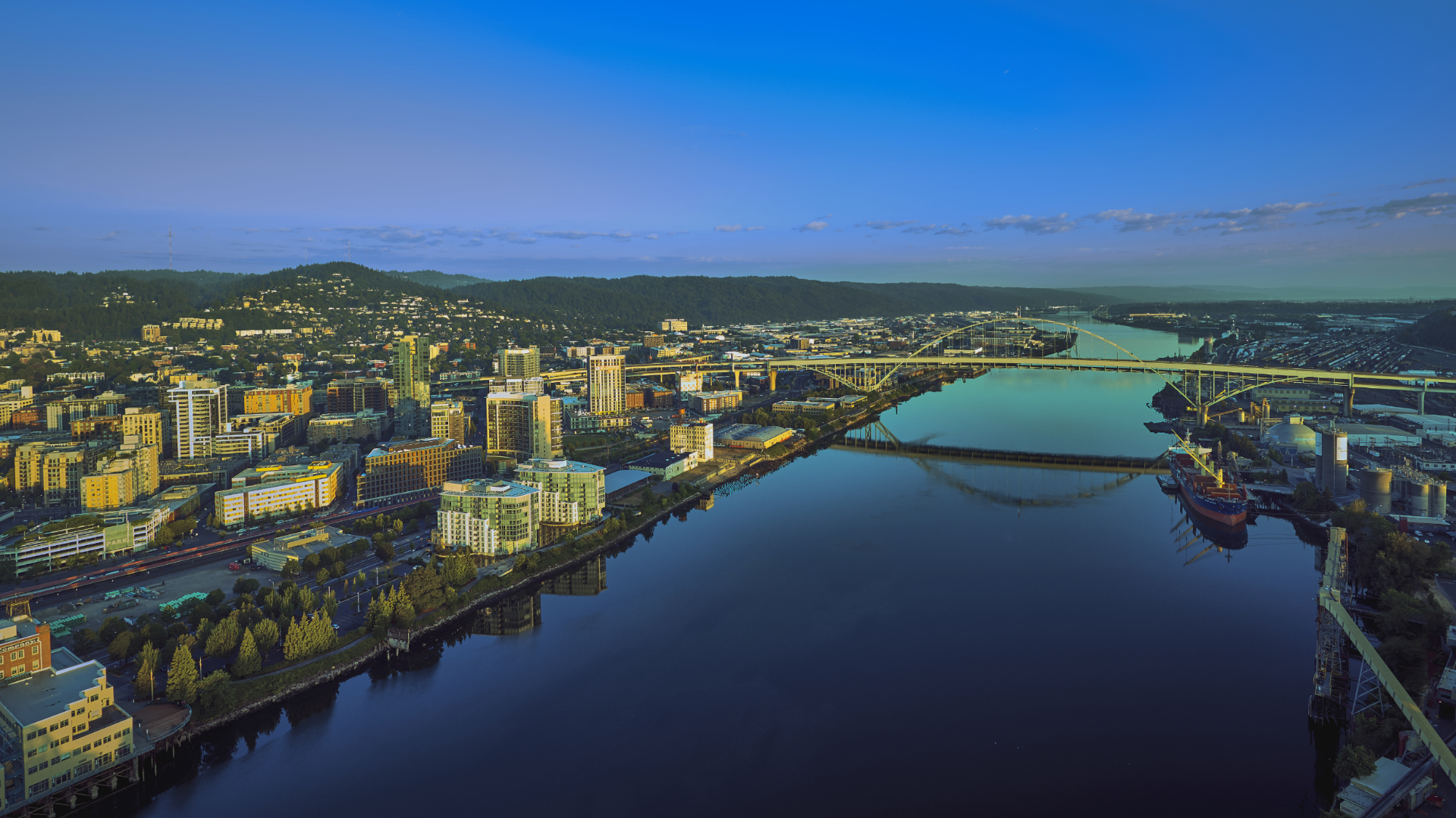 Drone aerial sunrise panorama of Portland waterfront with a ship loading cargo and the Fremont Bridge reflecting off the Willamette River Drone aerial sunrise panorama of Portland waterfront with a ship loading cargo and the Fremont Bridge reflecting off the Willamette River