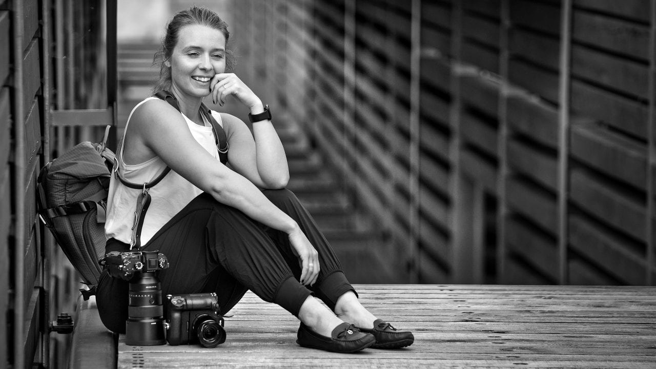 Female photographer with camera and prime lenses smiling